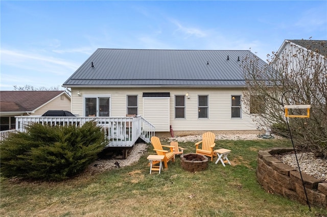 back of house with a standing seam roof, a deck, a fire pit, and metal roof