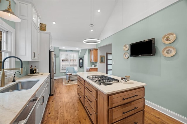 kitchen with light wood finished floors, a kitchen island, a sink, white cabinets, and appliances with stainless steel finishes