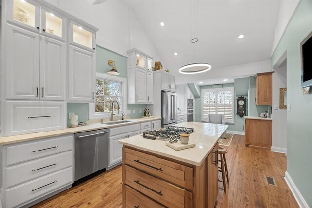 kitchen with a breakfast bar, a sink, stainless steel appliances, glass insert cabinets, and light wood-type flooring