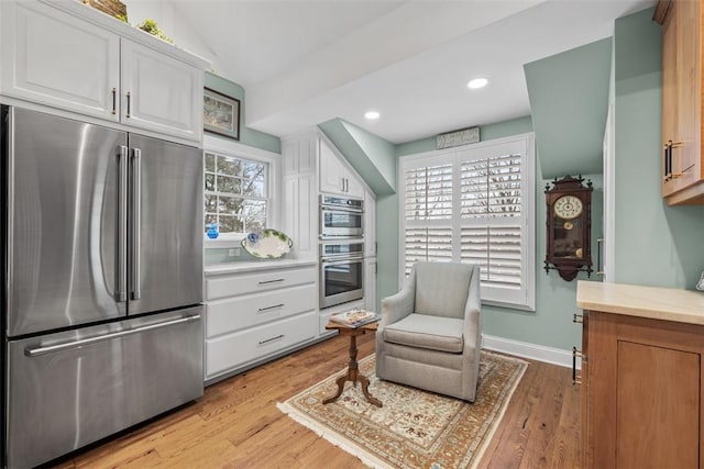 kitchen featuring stainless steel appliances, light countertops, white cabinets, vaulted ceiling, and light wood-type flooring