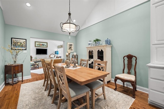 dining space with baseboards, light wood-style floors, and vaulted ceiling