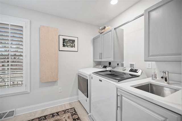 laundry room with visible vents, light wood-style flooring, separate washer and dryer, cabinet space, and a sink