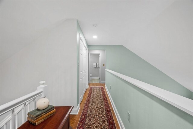 hall with wood finished floors, an upstairs landing, and baseboards