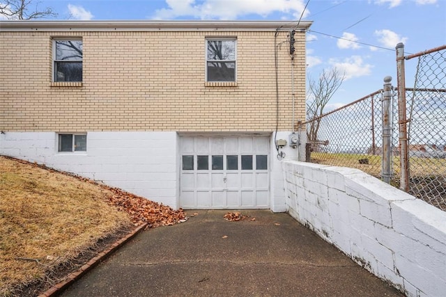 view of property exterior with aphalt driveway, an attached garage, brick siding, and fence