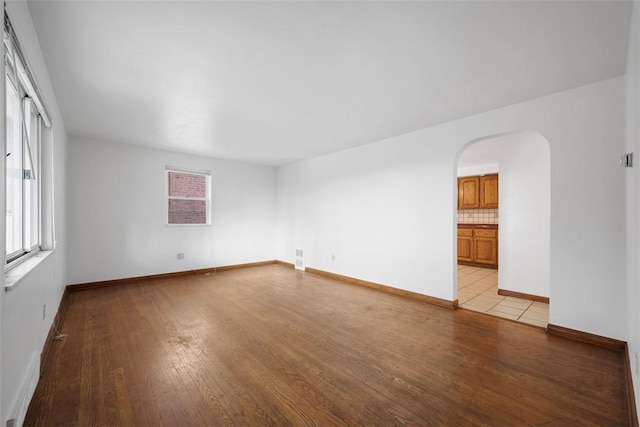 spare room featuring light wood-style floors, arched walkways, and baseboards