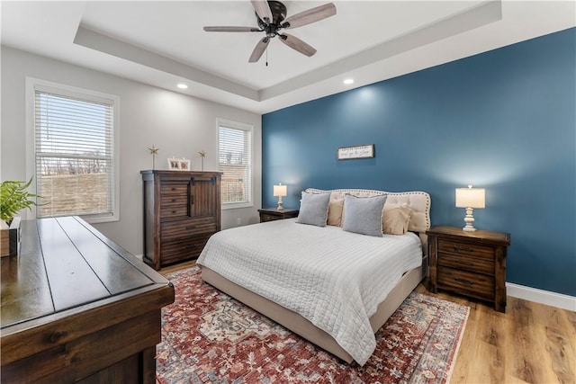 bedroom featuring a raised ceiling, recessed lighting, wood finished floors, and baseboards