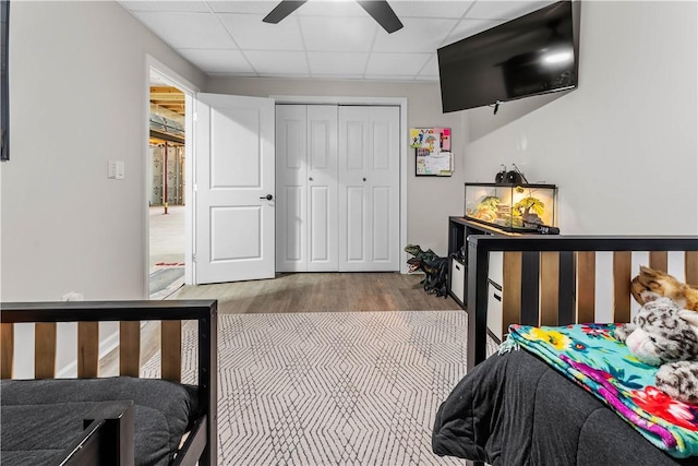 bedroom featuring a ceiling fan, wood finished floors, a paneled ceiling, and a closet