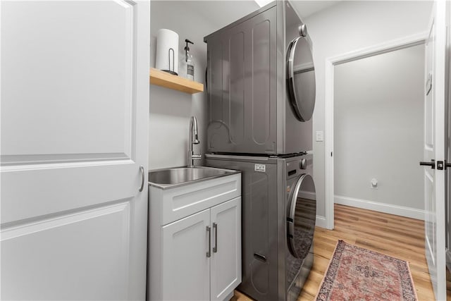 washroom with baseboards, stacked washer and dryer, light wood-style flooring, cabinet space, and a sink