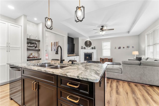 kitchen featuring a sink, a glass covered fireplace, open floor plan, a raised ceiling, and dishwasher