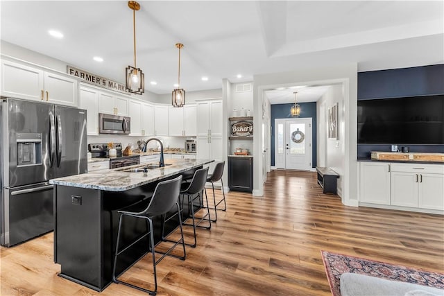 kitchen featuring a breakfast bar area, light stone counters, a sink, stainless steel appliances, and white cabinets