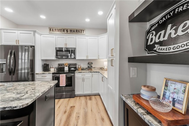 kitchen with light stone countertops, light wood-style floors, appliances with stainless steel finishes, and white cabinets