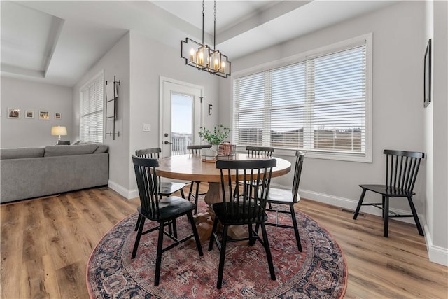 dining room featuring a notable chandelier, baseboards, light wood-type flooring, and a tray ceiling