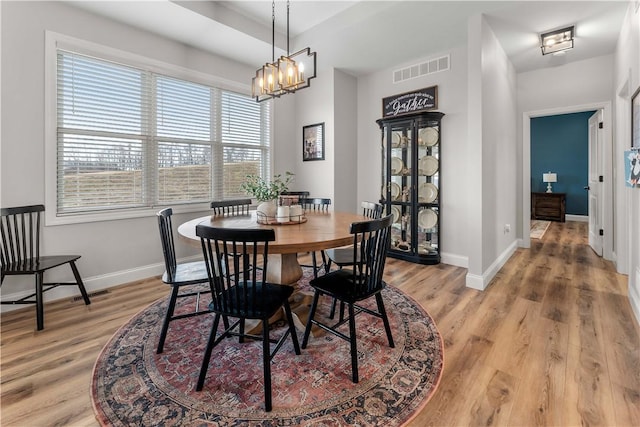 dining area featuring visible vents, light wood-style floors, baseboards, and a chandelier