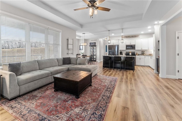 living area with baseboards, a tray ceiling, recessed lighting, light wood-style flooring, and a ceiling fan