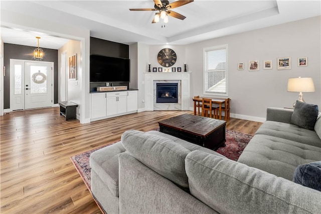 living area featuring light wood-type flooring, a raised ceiling, baseboards, and a high end fireplace