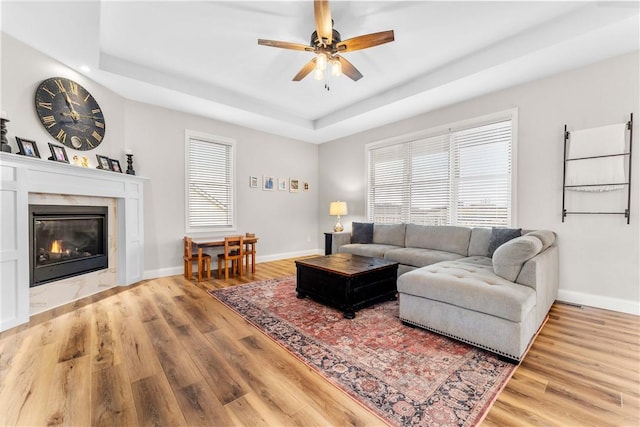 living area featuring a glass covered fireplace, light wood-style flooring, a raised ceiling, and baseboards