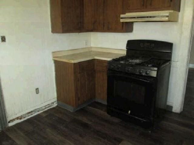 kitchen with under cabinet range hood, light countertops, dark wood-style flooring, and black gas stove