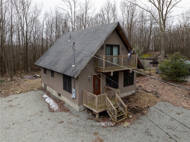 rustic home featuring a balcony, driveway, and a shingled roof