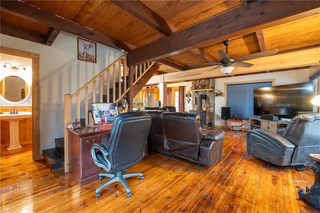 living area with beam ceiling, hardwood / wood-style flooring, stairway, wooden ceiling, and a wood stove