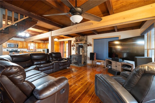 living area featuring beam ceiling, a wood stove, ceiling fan, and wood-type flooring