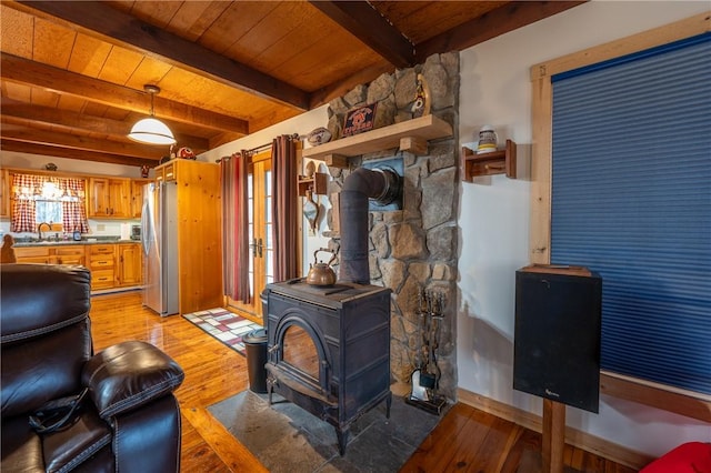 living room with light wood-type flooring, beamed ceiling, wooden ceiling, baseboards, and a wood stove