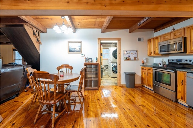 dining space with visible vents, light wood-type flooring, beam ceiling, stacked washer and clothes dryer, and an inviting chandelier