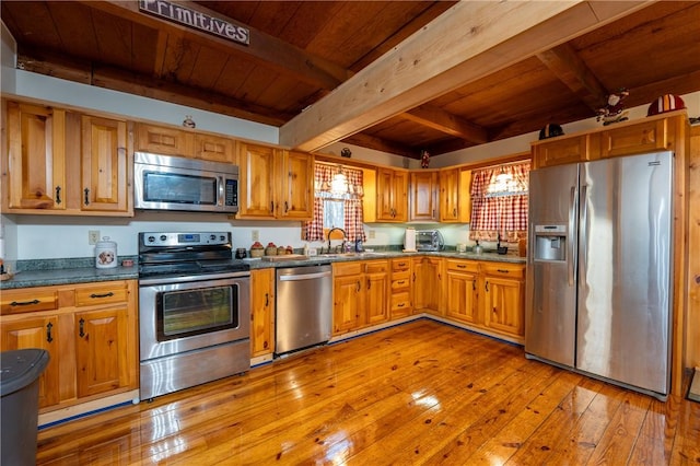 kitchen featuring light wood finished floors, a sink, wood ceiling, appliances with stainless steel finishes, and beamed ceiling