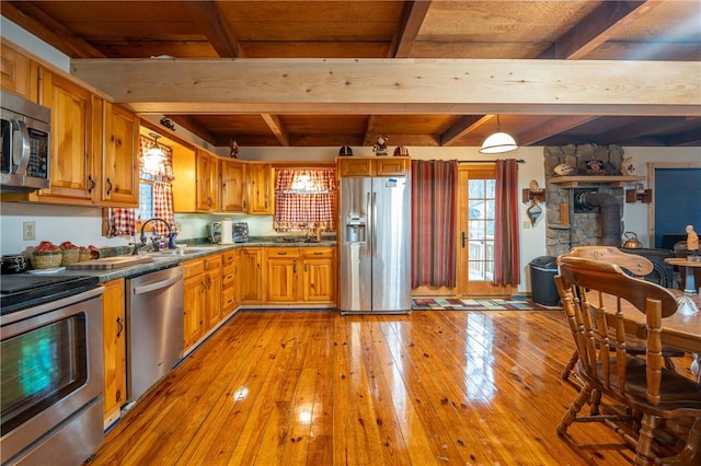 kitchen with beam ceiling, brown cabinets, a sink, stainless steel appliances, and light wood finished floors