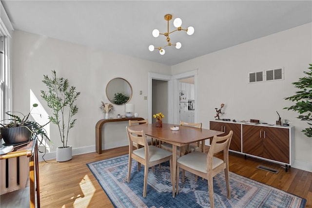 dining space featuring visible vents, wood finished floors, baseboards, and a chandelier