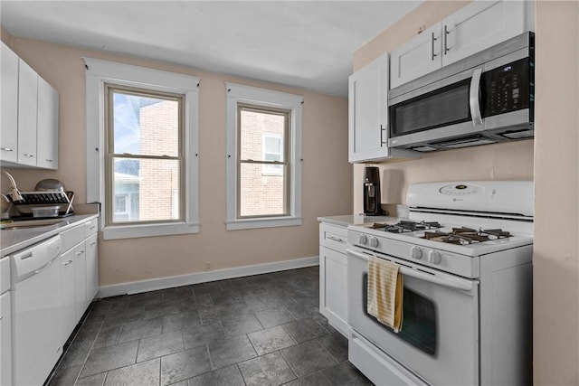 kitchen featuring white appliances, baseboards, a sink, light countertops, and white cabinetry