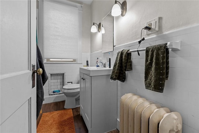 bathroom with vanity, radiator, wood finished floors, tile walls, and toilet