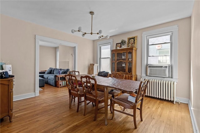 dining space with radiator, cooling unit, baseboards, light wood-style flooring, and a chandelier