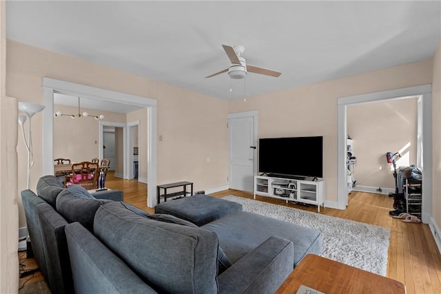 living area featuring baseboards, light wood-style floors, and ceiling fan with notable chandelier