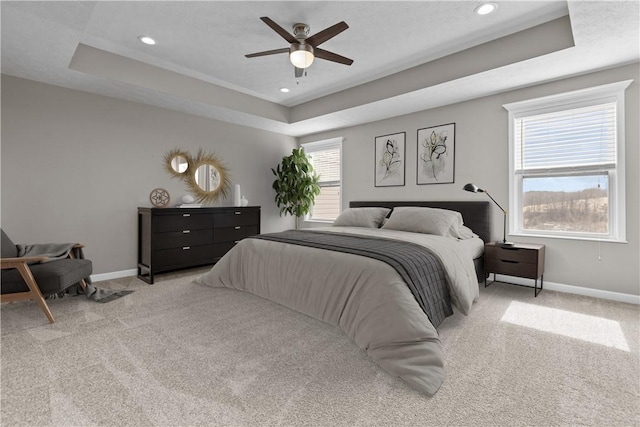 bedroom featuring a raised ceiling, baseboards, and light carpet