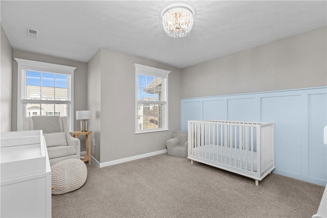 bedroom featuring visible vents, a textured ceiling, carpet floors, a decorative wall, and a chandelier