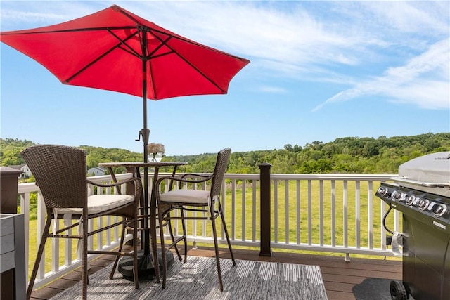 wooden deck featuring a lawn, a grill, a wooded view, and outdoor dining space