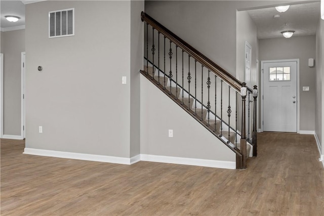 foyer featuring wood finished floors, baseboards, visible vents, stairs, and crown molding