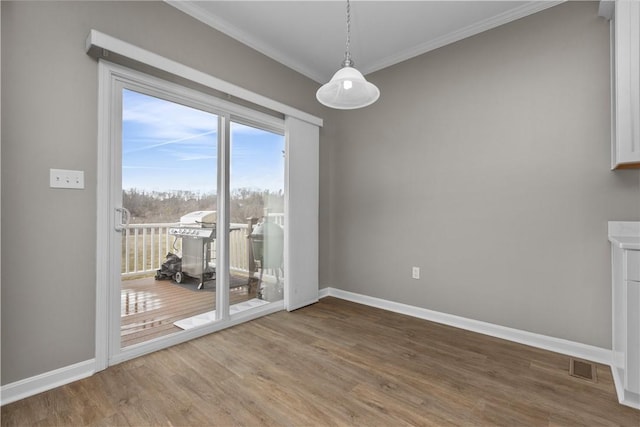 unfurnished dining area featuring visible vents, ornamental molding, baseboards, and wood finished floors