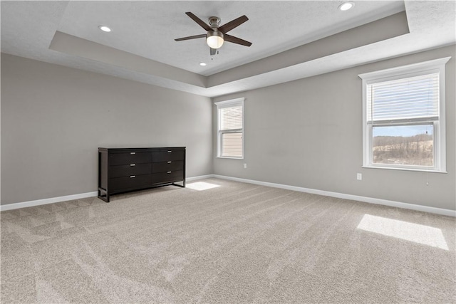 unfurnished bedroom featuring a tray ceiling, baseboards, and carpet flooring