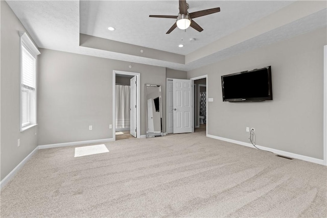 interior space featuring light colored carpet, a raised ceiling, and baseboards