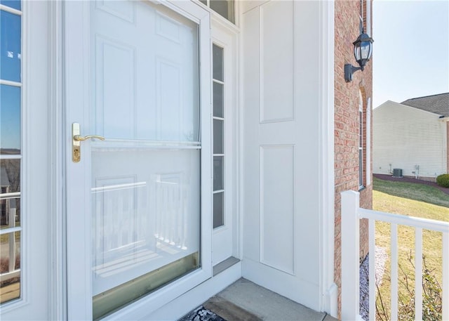 property entrance featuring brick siding, central AC unit, and board and batten siding