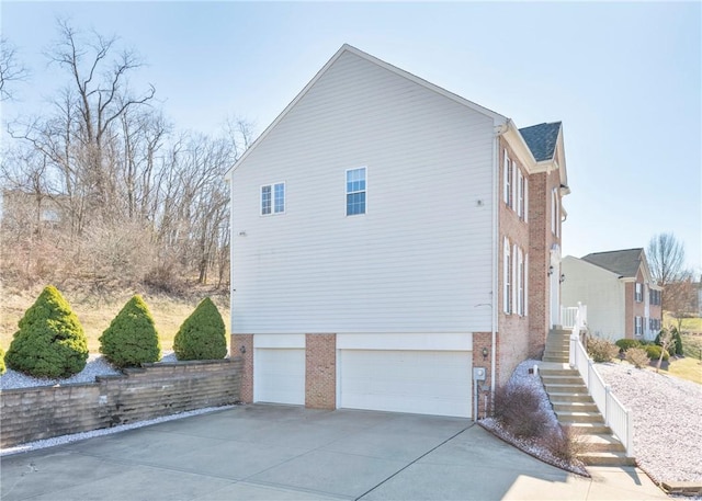 view of side of property featuring stairway, driveway, brick siding, and an attached garage