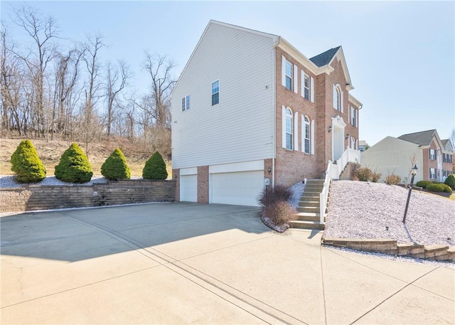 view of property exterior featuring stairs, an attached garage, brick siding, and driveway