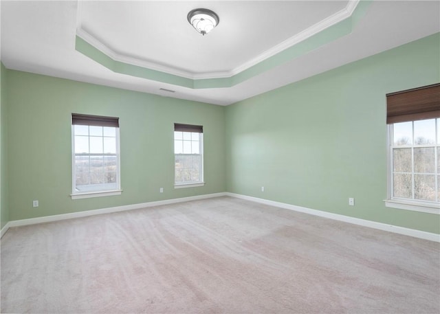 carpeted empty room featuring a tray ceiling, baseboards, and crown molding