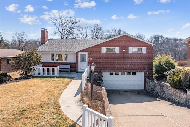 tri-level home with driveway, a front lawn, an attached garage, brick siding, and a chimney