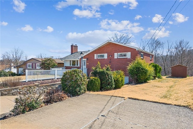 exterior space with fence, a chimney, an outdoor structure, a storage unit, and brick siding