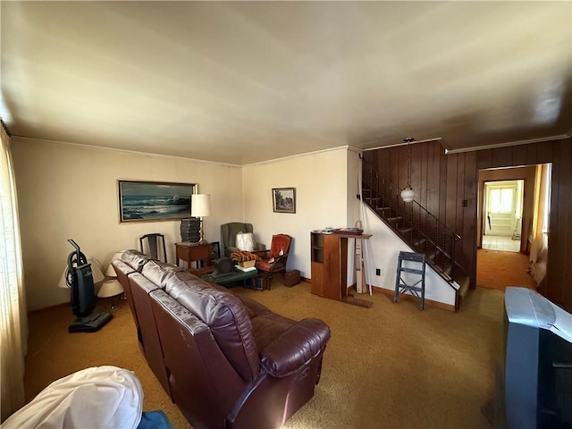 carpeted living area featuring stairway, baseboards, and wood walls