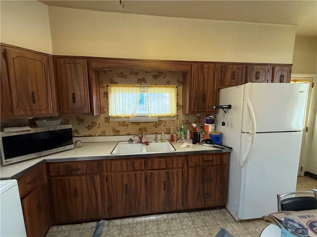 kitchen featuring stainless steel microwave, light floors, light countertops, freestanding refrigerator, and a sink