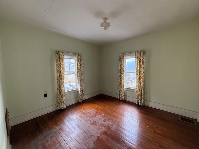 empty room with a wealth of natural light, visible vents, baseboards, and wood-type flooring