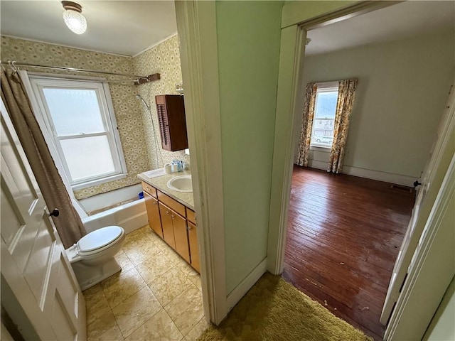 bathroom with toilet, shower / tub combo, wallpapered walls, baseboards, and vanity